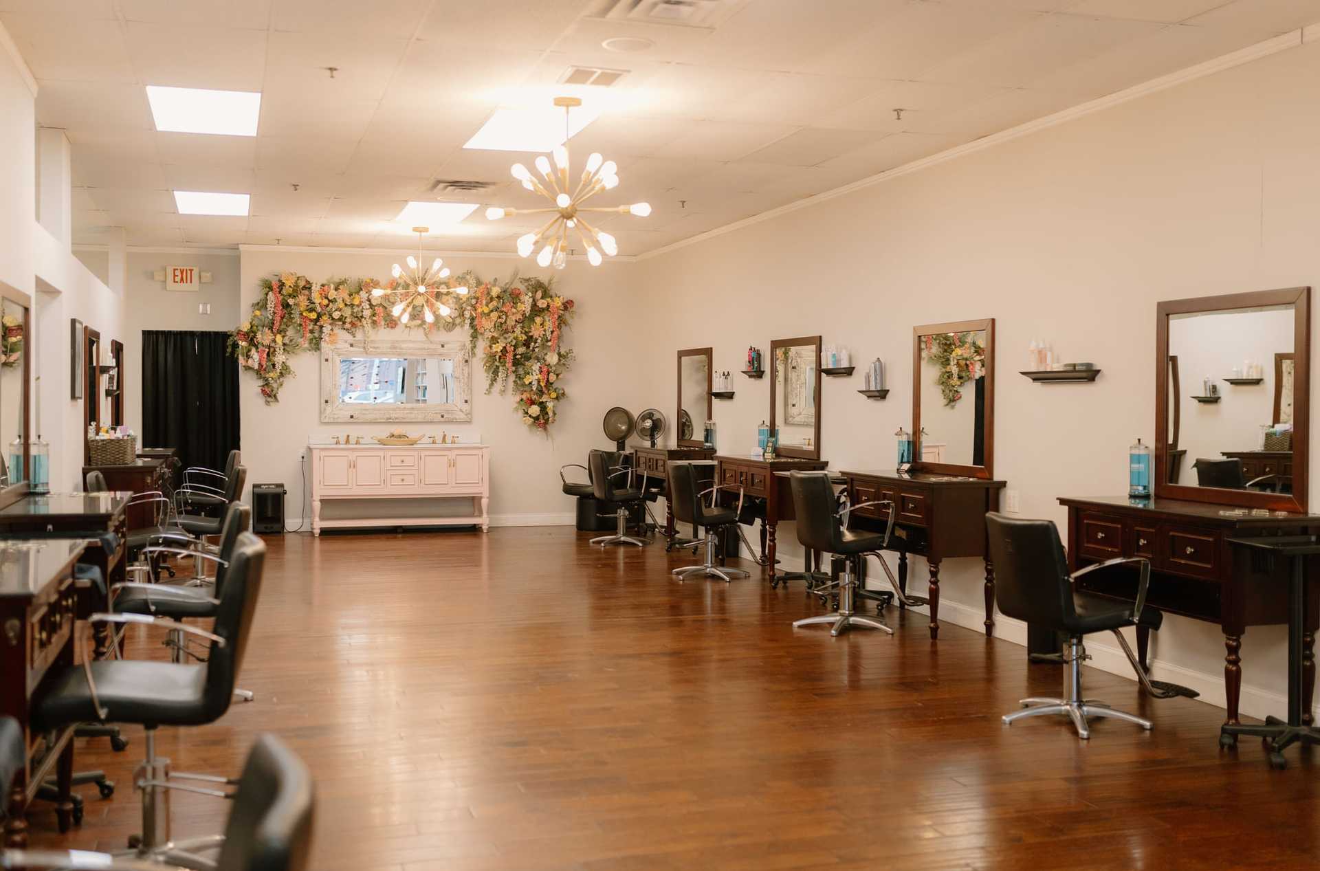Modern hair salon with mirror stations, floral decor, and wooden flooring.